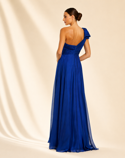 A woman models a floor-length one-shoulder evening gown in a rich royal blue, styled with clear high-heeled sandals against a warm cream studio backdrop. Royal blue one-shoulder floor-length evening gown for women