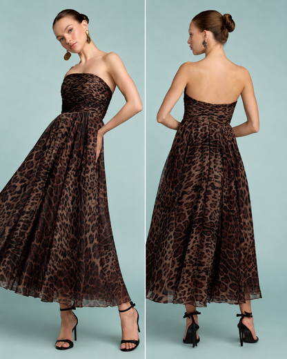 A woman modeling a strapless maxi dress with a brown and black leopard print pattern against a light blue background. Strapless brown and black leopard print maxi dress