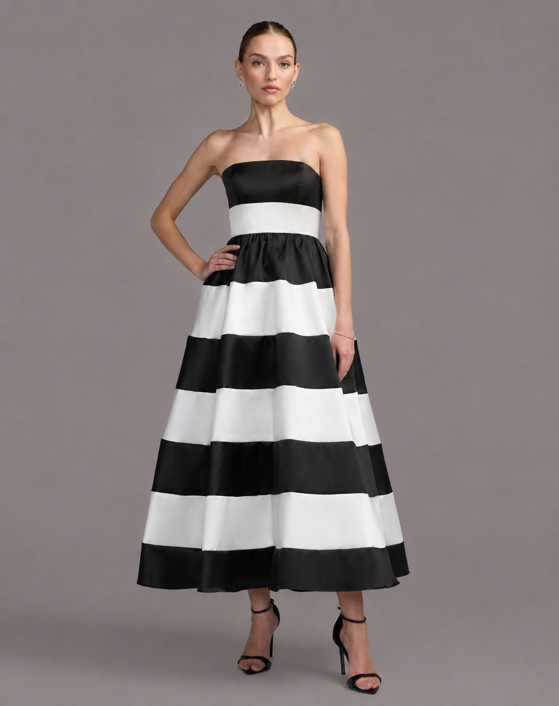 A woman modeling a strapless black and white striped maxi dress against a solid gray studio background. Black and white striped strapless maxi dress for women