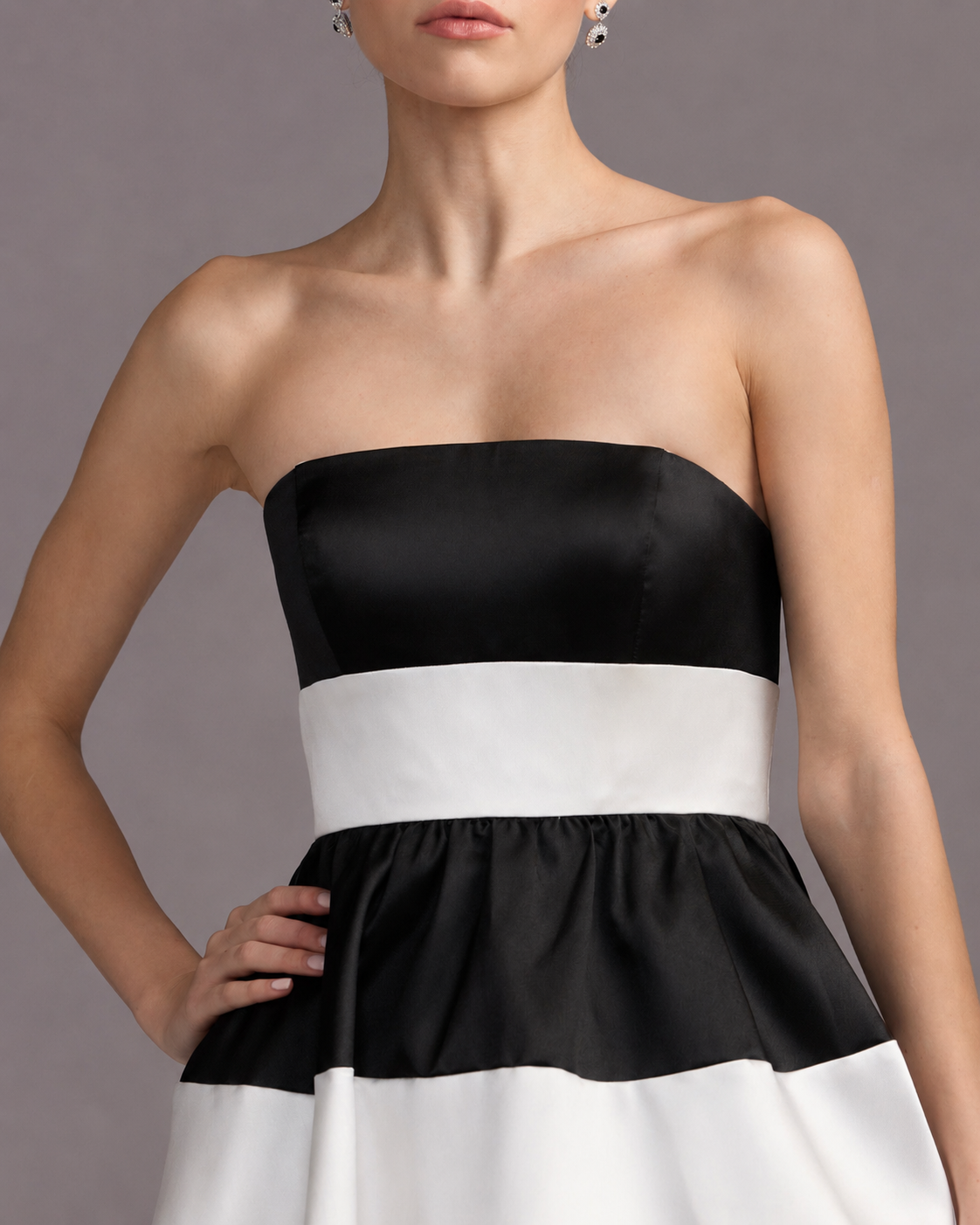 A woman wearing a strapless black and white color-blocked dress made of shiny satin-like fabric, shown from the mouth down against a plain gray studio background. Black and white striped strapless maxi dress for women