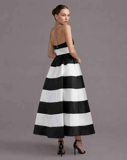 A woman modeling a strapless A-line maxi dress with bold horizontal black and white stripes, shown from the back against a solid gray studio background. Black and white striped strapless maxi dress for women