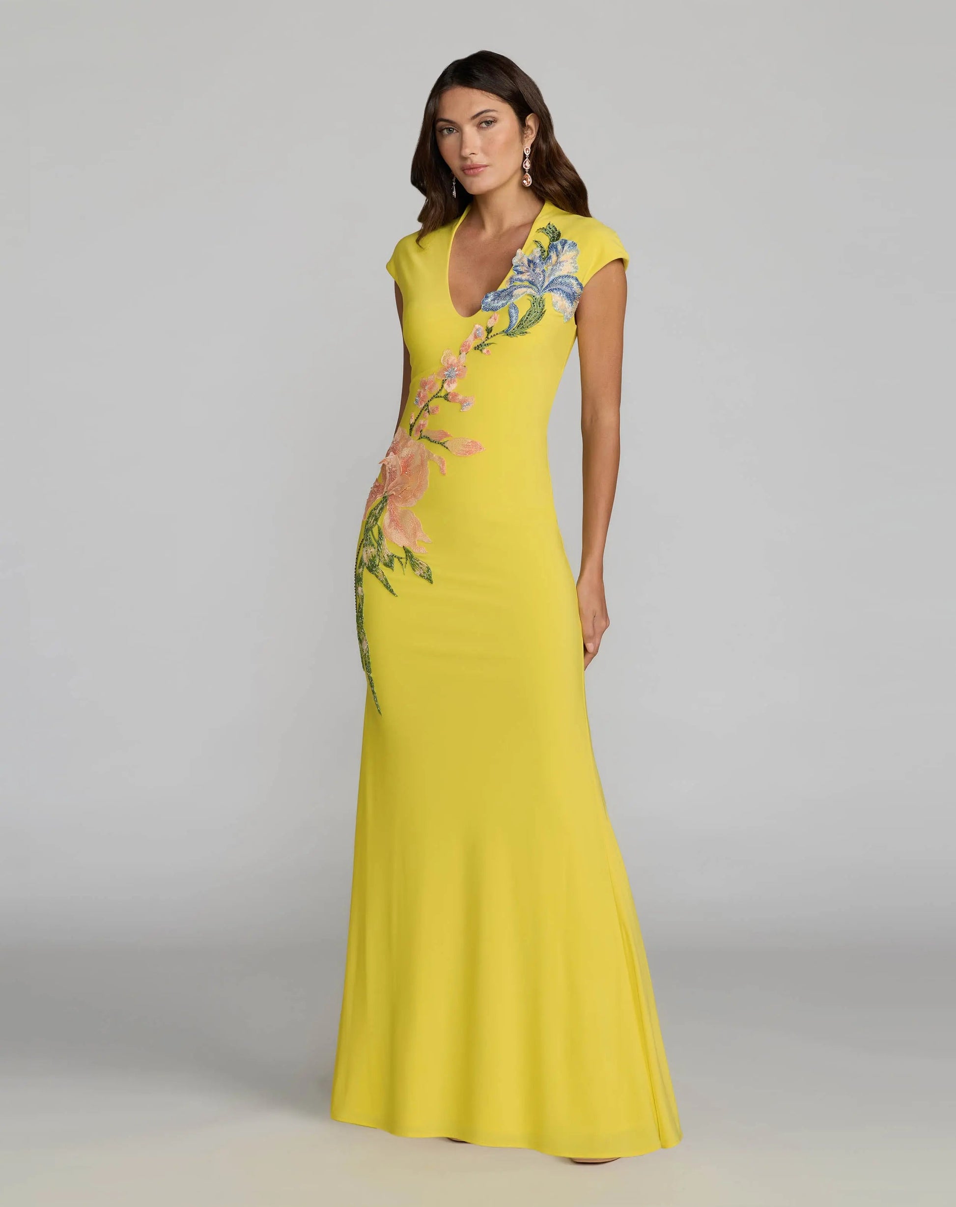Woman wearing a yellow evening gown with floral embroidery on a gray background. Yellow maxi dress with floral embroidery for women. Yellow maxi dress with floral embroidery for women