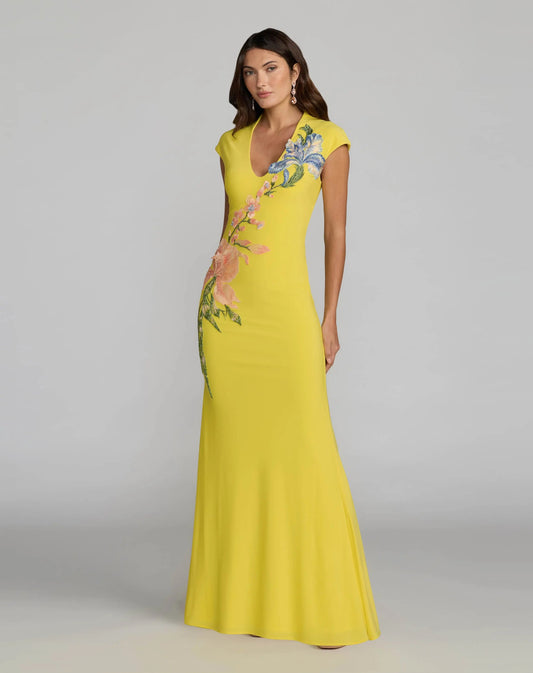 Woman wearing a yellow evening gown with floral embroidery on a gray background. Yellow maxi dress with floral embroidery for women. Yellow maxi dress with floral embroidery for women