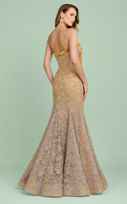 A woman modeling a strapless floor-length mermaid gown from the back, featuring a gold and taupe floral jacquard pattern against a solid sage green studio background. Gold and lavender floral strapless mermaid gown with satin bow